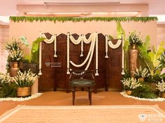 a chair sitting in front of a wall decorated with flowers and greenery for a wedding ceremony