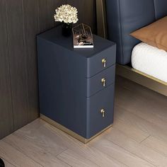 a nightstand with a flower on it next to a bed and night stand in a bedroom