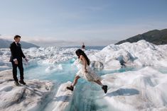 a man and woman are standing on the edge of an ice - covered lake with blue water