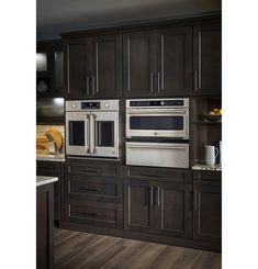 a kitchen with dark wood cabinets and stainless steel ovens in the center, along with white counter tops