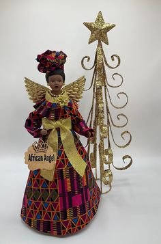 "Celebrate pride and beauty with our unique AFRICAN ANGEL Tree Topper and give your loved ones the gift of representation that reflects images of you and your family. Our Beautiful Angel Tree Topper add the perfect final touch to your Christmas, Kwanzaa and Home Decorating. (Please see listings for other available styles, as seen in the collection photo: Purple, Baby Blue, Pink and Blue Metallic Gold colors). OPTIONAL: Clear Display Case Let me tell you more about this AFRICAN ANGEL (Dressed in African Angel, Christmas Tree Angel, Metallic Gold Color, Angel Tree Topper, Angel Dress, Angel Tree, Kwanzaa, Ankara Fabric, Gold Ribbons