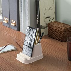 a desk with a cell phone, pen and pencil holder on it next to some books