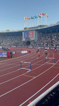 two women running on a track in front of an audience at a sporting event with flags