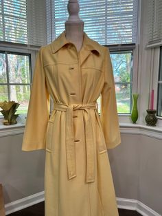 Sweet little Weather Charmer trench style coat, perfect for Spring/Easter attire.  A beautiful pale yellow, this lightweight coat features side pockets and a sash belt.  Its very Audrey Hepburn/Mary Tyler Moore!  Inside label does not give me the fabric content, however it does say handwash. It is a lightweight linen style fabric; please see photos for further description and note photo #4 some loose stitching under Left arm and belt, also photo #5 light stain on sleeve. I used Woolite At Home D Vintage Long Spring Outerwear, Vintage Long Beige Outerwear, Retro Beige Outerwear For Spring, Retro Beige Spring Outerwear, Retro Cream Outerwear For Spring, Vintage Beige Outerwear For Daywear, Vintage Spring Daywear Outerwear, Vintage Spring Outerwear For Daywear, Vintage Fitted Yellow Outerwear