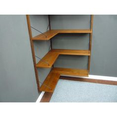 an empty shelf in the corner of a room with carpet on the floor and gray walls