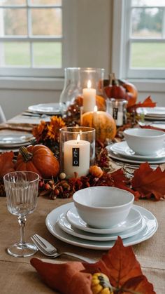 the table is set with white dishes and candles