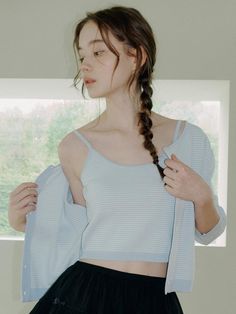 a woman with long hair standing in front of a window wearing a blue shirt and black skirt