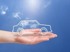 a hand holding a paper cutout of a car in the sky with clouds behind it