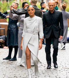 a man and woman walking down a street with people in the background wearing black suits