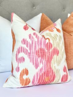 three pillows on a bed with white sheets and pink and orange designs in the middle