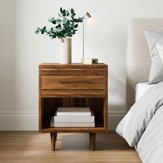 a nightstand with two books and a plant on it next to a bed in a bedroom