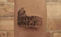 a tattoo on the leg of a person with a building in the background and a brick wall behind it