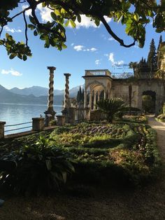 an outdoor garden area next to a body of water with mountains in the background and trees on either side