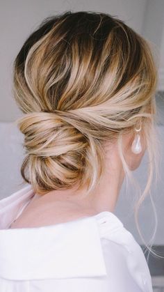 a woman with blonde hair styled into a low bun, wearing a white blouse and pearl earrings