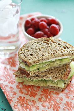 a sandwich with avocado, cucumber and raspberries next to a glass of water