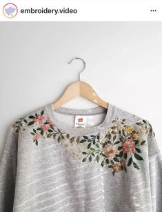 a gray sweater with flowers on it hanging from a hanger