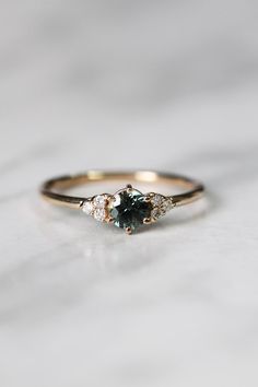 an engagement ring with two diamonds and a green tourmaline in the center on a marble surface