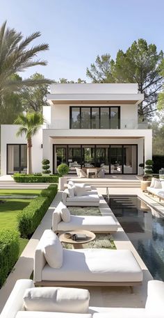 an outdoor living area with white couches and green grass in front of the house