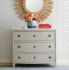 a white dresser with flowers on top and a mirror above it in front of a polka dot wall