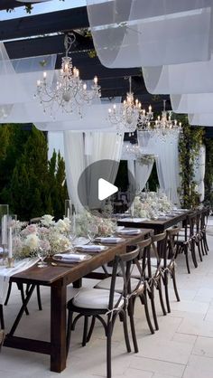 an outdoor dining area with white curtains and chandeliers