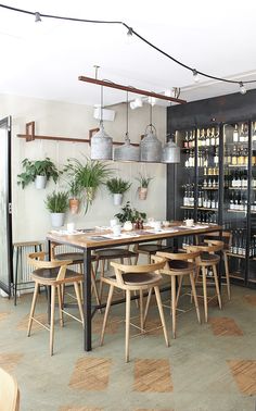 a dining room with wooden chairs and plants on the wall above it, along with shelves full of wine bottles