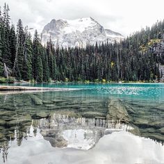 a lake surrounded by trees and mountains with snow on the mountain in the back ground