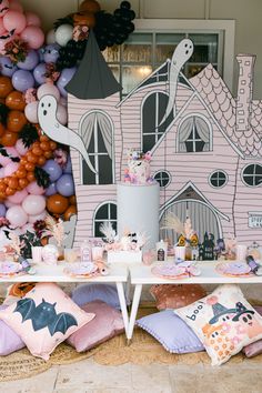 a table topped with lots of pink and purple balloons next to a halloween themed house