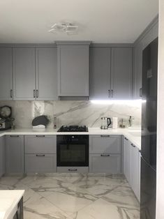 a kitchen with marble counter tops and gray cabinets, along with an oven in the middle