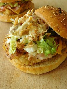 two sandwiches with chicken, lettuce and cheese on them sitting on a wooden surface