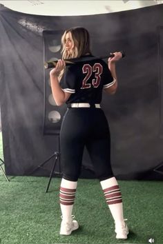 a woman is standing in front of a backdrop holding a baseball bat and posing for the camera