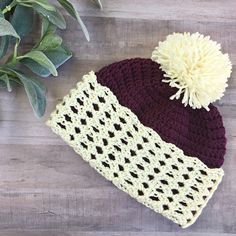 a crocheted hat with a pom - pom sits next to a potted plant