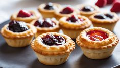 small tarts with jam and jelly fillings on a black plate next to raspberries