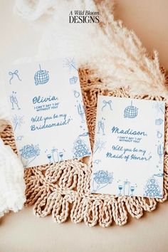 two blue and white wedding stationery cards on a lace doily next to a feather