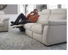 a man sitting on top of a white couch in a living room next to a gray rug