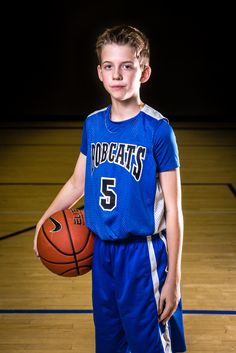 a young boy holding a basketball on top of a court