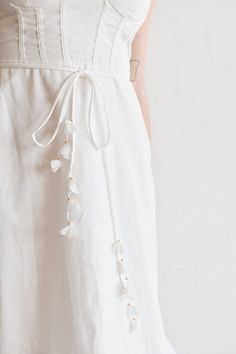 Quiet luxury meets high style in the Chiara White Buster-Style Midi dress. This makes a perfect summer engagement party dress for brides. This linen midi dress features a delicate 3D floral detailed belt that gives it that wow factor, a classic fit and flare skirt and bustier style top. Self tie shoulder straps. A smocked back helps it fit multiple bust sizes. Delicate White Dresses For Spring, Delicate White Spring Dress, Spring A-line Dress With Belt, Elegant A-line Maxi Dress With Tie Waist, Summer Floral Bridesmaid Dress, Floral Embellished A-line Midi Dress For Wedding, Elegant Floral Embellished Maxi Dress For Summer, Elegant Spring Maxi Dress With Belt, Elegant Spring Belted Maxi Dress