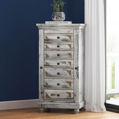 an old white chest of drawers in front of a blue wall