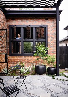 a person is looking out the window of a brick house with potted plants and chairs