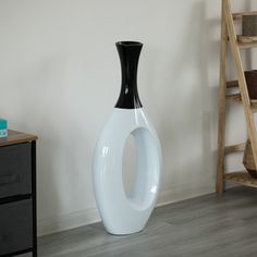 a black and white vase sitting on the floor next to a wooden shelf in a room