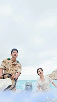 a man and woman in uniform standing next to each other near the ocean while holding a steering wheel