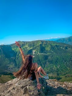 a woman with long hair sitting on top of a mountain