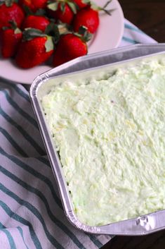 a pan filled with green frosting next to a plate of strawberries on a table