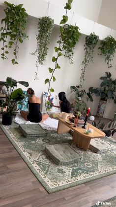 a woman sitting on top of a rug in front of a plant filled living room