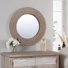 a round mirror on top of a dresser next to a vase with flowers in it