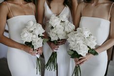 three women in white dresses holding bouquets of flowers