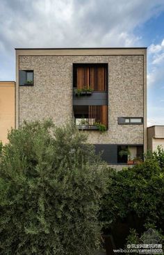 an apartment building with trees and bushes in front of the windows, on a cloudy day