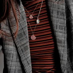 a woman wearing a black and white checkered blazer with two necklaces on her neck