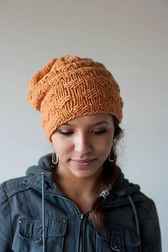 a woman wearing an orange knitted hat and looking at her cell phone while standing in front of a white wall