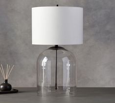 a lamp that is on top of a table next to a small black object and a white lampshade