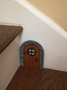 a small door in the corner of a room next to a wooden floor and stairs